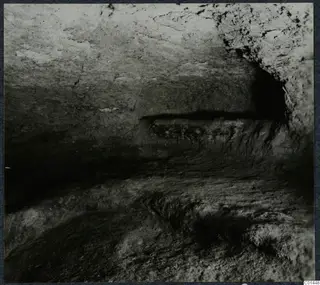 Interior of Tomb 14 at Ayios Iakovos, showing rough-cut rock walls, a low ledge and a dark recess