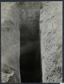 Narrow cut in excavated soil leading down to a dark opening, Tomb 12 at Ayios Iakovos during excavation