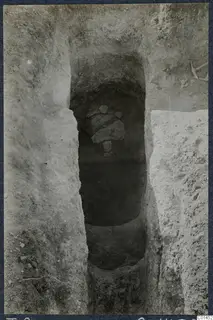 Tomb 8 at Ayios Iakovos during excavation, with stone slabs in the chamber opening and a pick at the top right