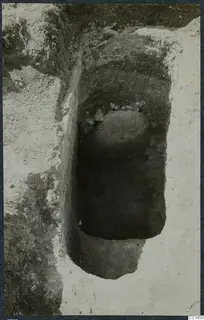 Excavated tomb at Ayios Iakovos: a rounded stone and small stones sit in a narrow cut in the soil.