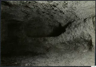 Interior of Tomb 14 at Ayios Iakovos, a rock-cut chamber with rough walls and loose debris on the floor.