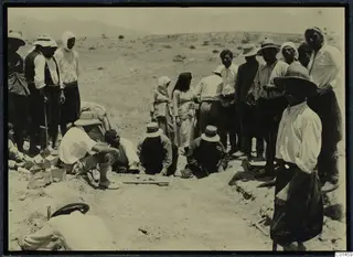Workers and onlookers in wide hats gathered around an excavation trench at Ayios Iakovos
