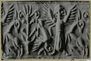 Enlarged photograph of a carved stone seal with a standing robed figure, a tall stylised plant and winged figures in relief