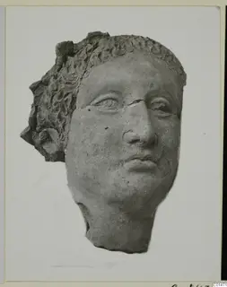 Head fragment of a statue with curled hair in relief and a broken nose, shown on a mounted card
