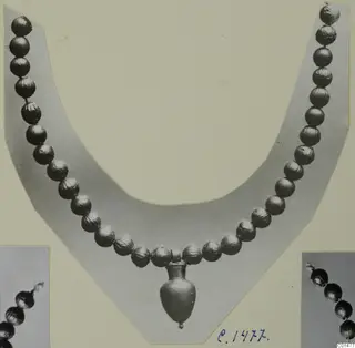 Necklace of metallic beads with a small vase-shaped pendant, shown on a card mount with two close-up views