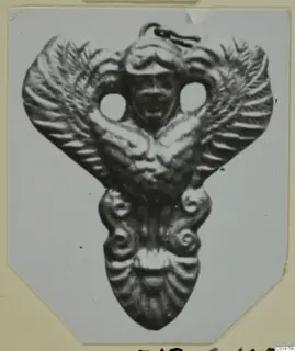 Gold pendant from Marion with a central face between spread wings and spiral motifs below