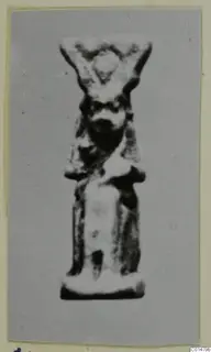 Small standing figure amulet, probably faience, from tombs at Marion, photographed on a grey card mount.