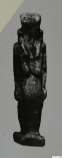Small standing figure from Marion Tomb 50, dark with pale speckled patches, shown against a plain grey backdrop.