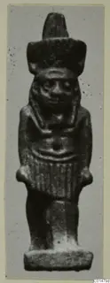 Small dark figurine named Nefertum, with a tall headdress, standing on a flat rectangular base.