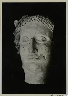 Head of a figure with carved curls, a chipped nose and a cracked mouth, photographed against a black background.