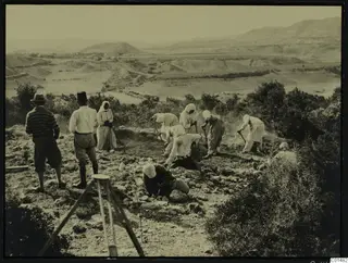 Workers digging with hoes at the excavation at Palaeoskoutella, with hills and a valley behind