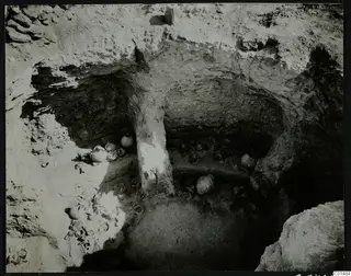 Rock-cut chamber at Nitovikla with pottery vessels and sherds lying on the floor during excavation.