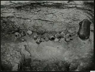 Pottery vessels lying in situ on the floor of an excavated cutting, with a large jar standing against the cut wall