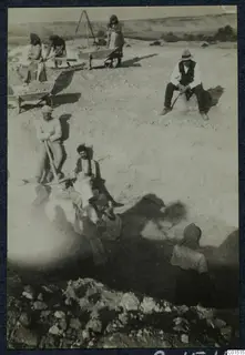 Workers digging at the Soli theatre excavation with picks and a wheelbarrow, with a heap of stones in front