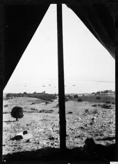 View through a tent opening over dry fields, scattered trees and the sea at Soli