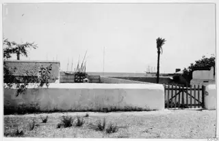 Whitewashed wall and wooden gate, with masted boats and the sea beyond, at Larnaca
