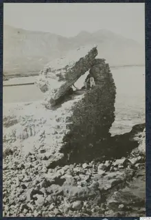 Man sitting in the shadow beneath a large overhanging stone block by the sea at Lambousa