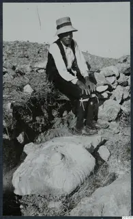 Seated man in a wide-brimmed hat beside a large stone block lying in an excavated trench at Vouni