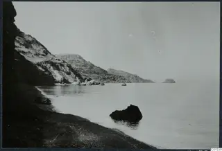 Rocky shoreline with a dark pebble beach, calm sea and a cliff at left, near Vouni.