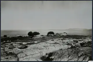 Small stone building and trees on rocky ground at Vouni, with the sea and distant hills behind