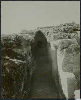 Excavated passage between rough stone walls, with an arched opening at the far end, at the Vouni palace