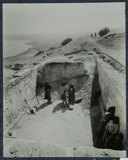 Room 93 at Vouni during excavation, with workers in a trench beside cut stone walls and the sea beyond