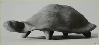 Terracotta figurine of a tortoise with a domed shell, four short legs and the head projecting to the left.