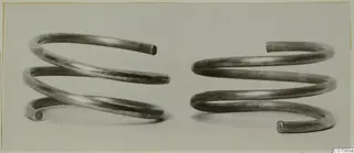 Two spiral silver armlets of round wire with open ends, shown side by side.