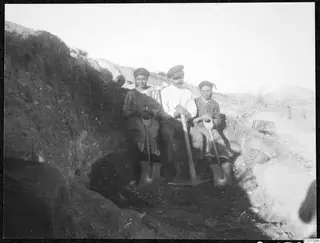 Solon and two workers seated in an excavation trench, holding a pickaxe and two spades against the trench wall.