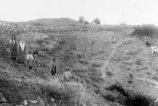 Grassy hillside at Soli before excavation, with a dry-stone wall across the slope and a group of people on the left.