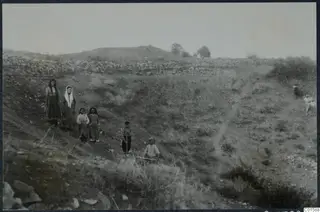 Theatre at Soli before excavation: a grassy slope with a stone wall, and a group of people in the foreground.