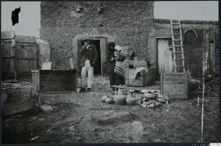 Packing pottery in a courtyard at Milia, with a man and a woman beside a mud-brick building