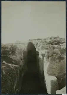 Excavated trench between cut stone walls at Vouni Palace, with a rounded opening in the far wall