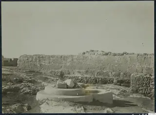 Long weathered wall at Vouni Palace with a circular stone base and broken stone blocks in the foreground