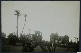 Ruined stone buildings and tall palm trees at Famagusta, seen across open grassy ground.
