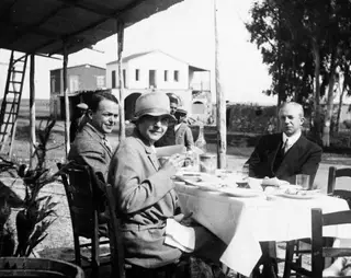 Erik Sjöqvist, Gudrun Atterman and John Lindros eating lunch at an outdoor table under a corrugated roof