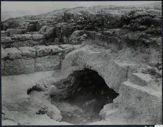 Excavation at Vouni palace showing rough stone walls and an arched rock-cut opening leading down into a dark hollow