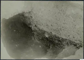 Close view of an excavation cutting at the palace at Vouni, with a pale hard surface above a dark hollow and layered soil.