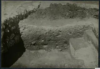 Excavation at the Vouni palace showing a low rubble wall and a stepped stone block beside a trench.
