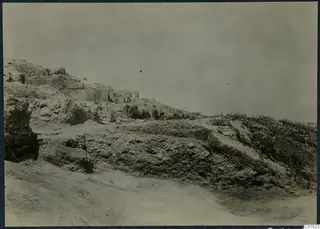 Ruined stone wall and rubble on a dry slope at the palace at Vouni, with grass growing along the top