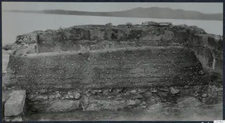 Ruined wall with layered pebbly fill and stones at the base, at the palace at Vouni, with hills behind
