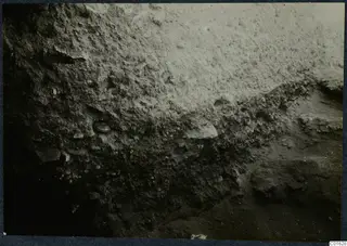 Excavated earth face with stones and a small round object at the palace at Vouni
