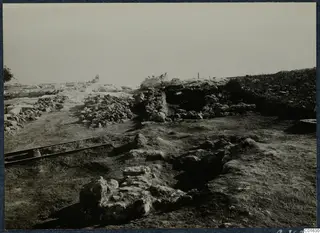 Excavated ruins at the palace at Vouni, with low stone walls, rubble and two rails in the foreground