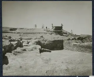 Excavated stone walls at Vouni palace, with a rail cart and several blurred figures on the ridge behind.