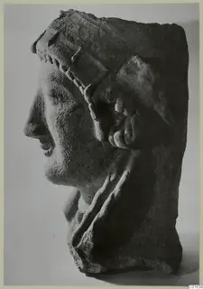 Profile of a carved head facing left, with a beaded band across the brow and a large curled ornament at the ear.