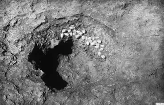 Small pale stones lying in an arc on excavated ground beside a dark hollow at Vouni Palace