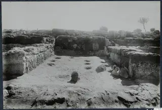 Excavated room at Vouni with stone walls, a pot standing on the floor and a handled jug at the right-hand wall.