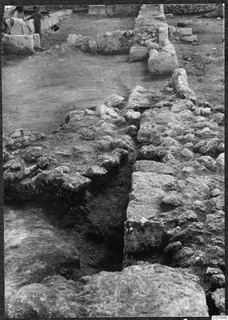 Excavated wall foundations and loose stones at Vouni Palace, with two people at the top left.