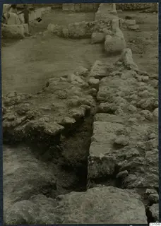 Stone wall foundations and a dug trench at Vouni Palace, with two people standing in the background at top left.