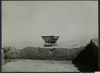 Iron cart standing on top of a long stone wall at Vouni Palace, with open sky and hazy land behind